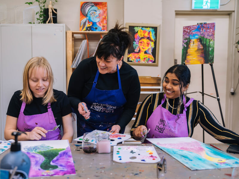 Two women having fun at a painting class with their teacher