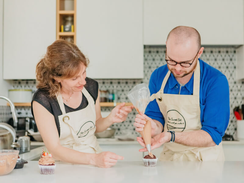 A son decorates a cupcake with his mother