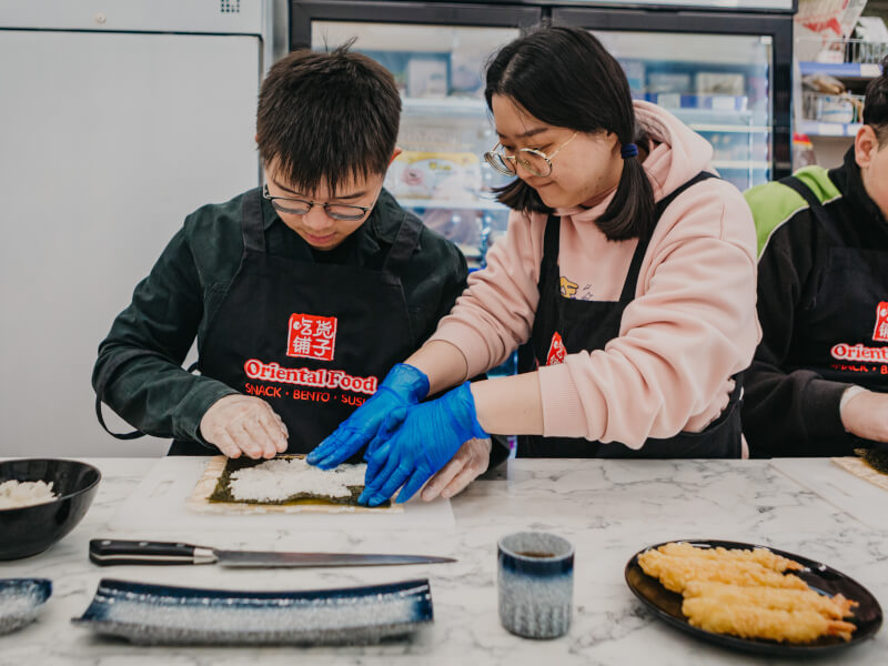 Cooking teacher helping student assemble sushi