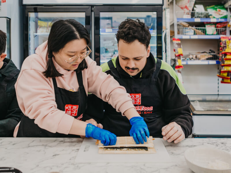 Chef helps student roll sushi at a sushi making class