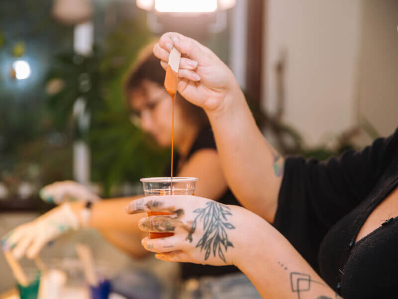 A tattooed hand pours paint at an abstract art class