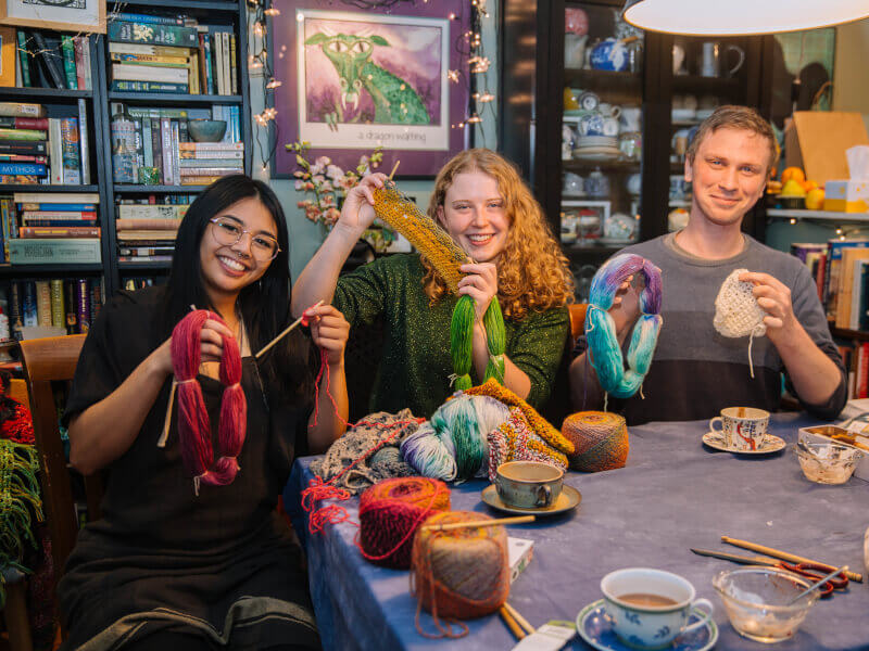 Three friends surrounded by yarn and knitting projects enjoying tea