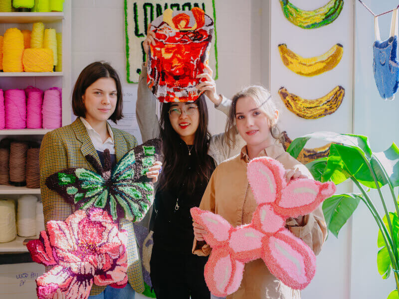 Three women holding their colourful tufted rugs