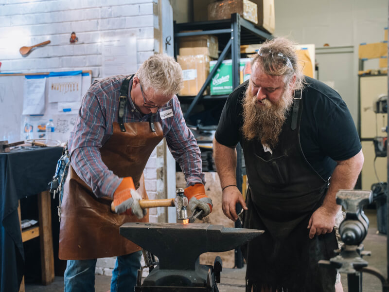 Two men laughing as they make knives during a gifted workshop