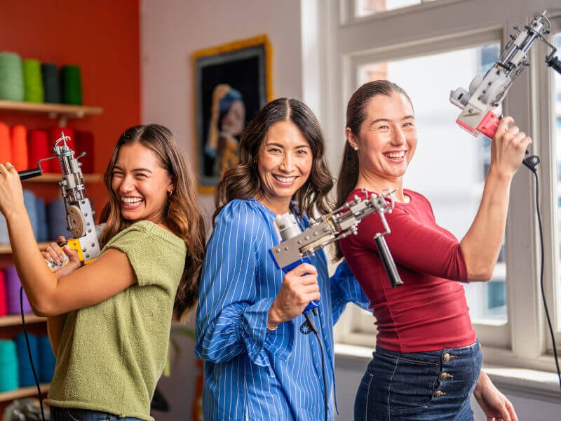 three women playfully ready to tuft with tufting guns