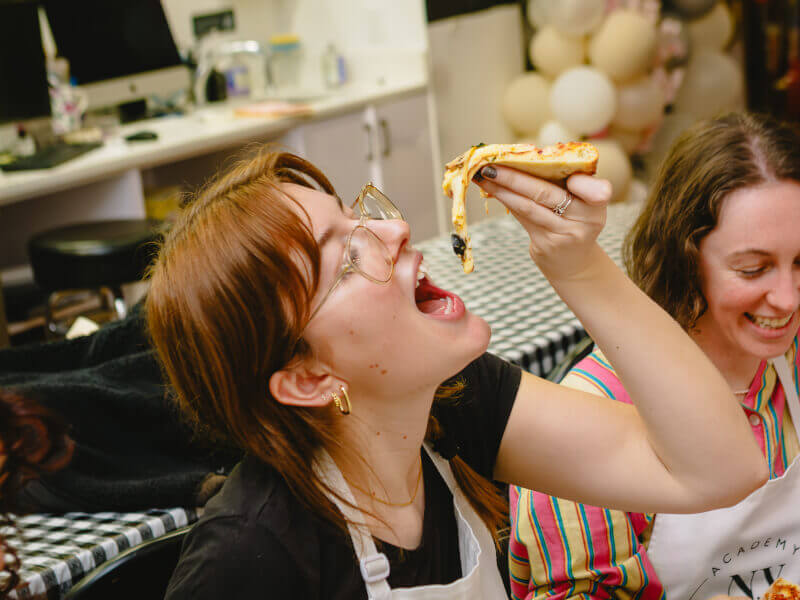 Woman tilts her head back to eat handmade pizza at lunch with friends in Perth