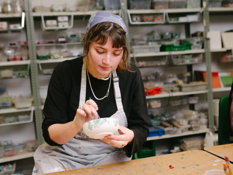 A woman paints her ceramic plate at a pottery class