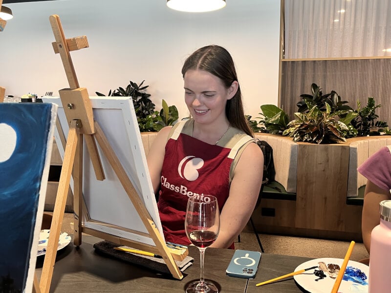 A woman enjoys a painting class with a glass of wine