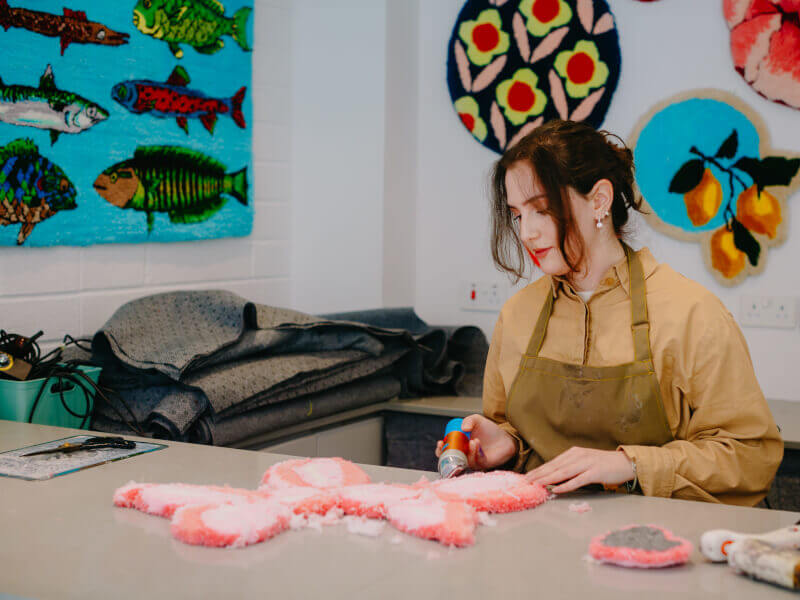 A woman making a rug in a colourful tufting studio