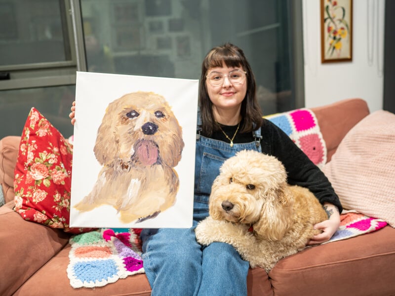 A woman poses with her dog and her hand-drawn pet portrait 