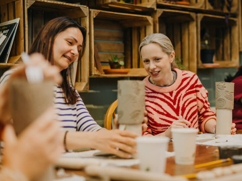 Two women handbuild clay vessels at a pottery class they were gifted for Mother's Day