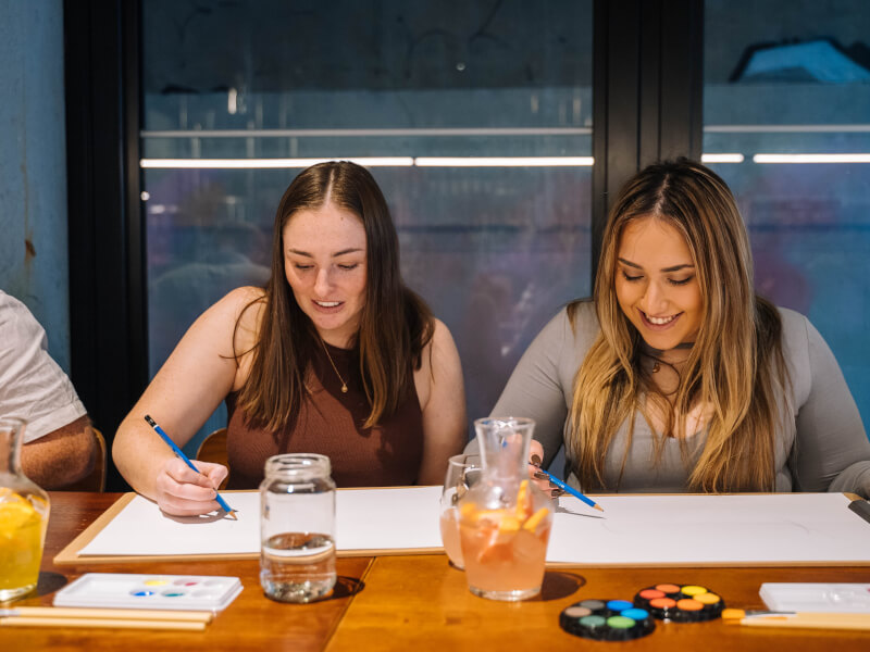 Two women painting with cocktails