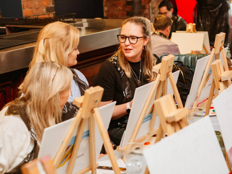 Three women catching up at a painting class